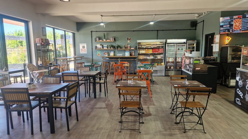 The seating area with bistro tables and chairs, a long window down one side and drinks fridges at the back